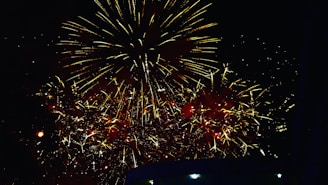 A dazzling burst of red and gold fireworks lighting up a dark night sky over a festive market.