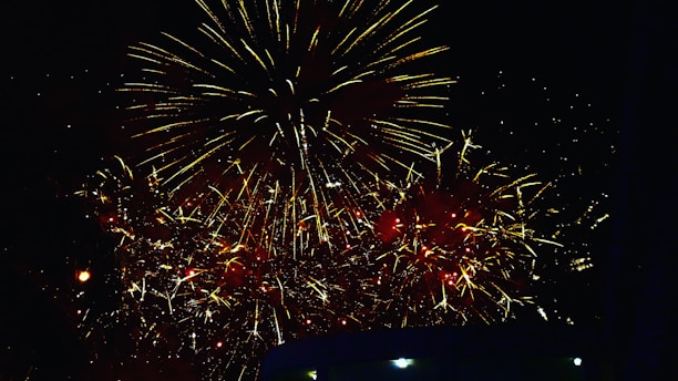 A dazzling burst of red and gold fireworks lighting up a dark night sky over a festive market.