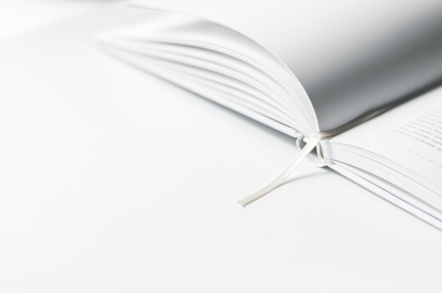 An open book with a white ribbon bookmark rests on a bright surface. The pages are crisp and the image is well-lit, conveying a sense of minimalism and cleanliness.