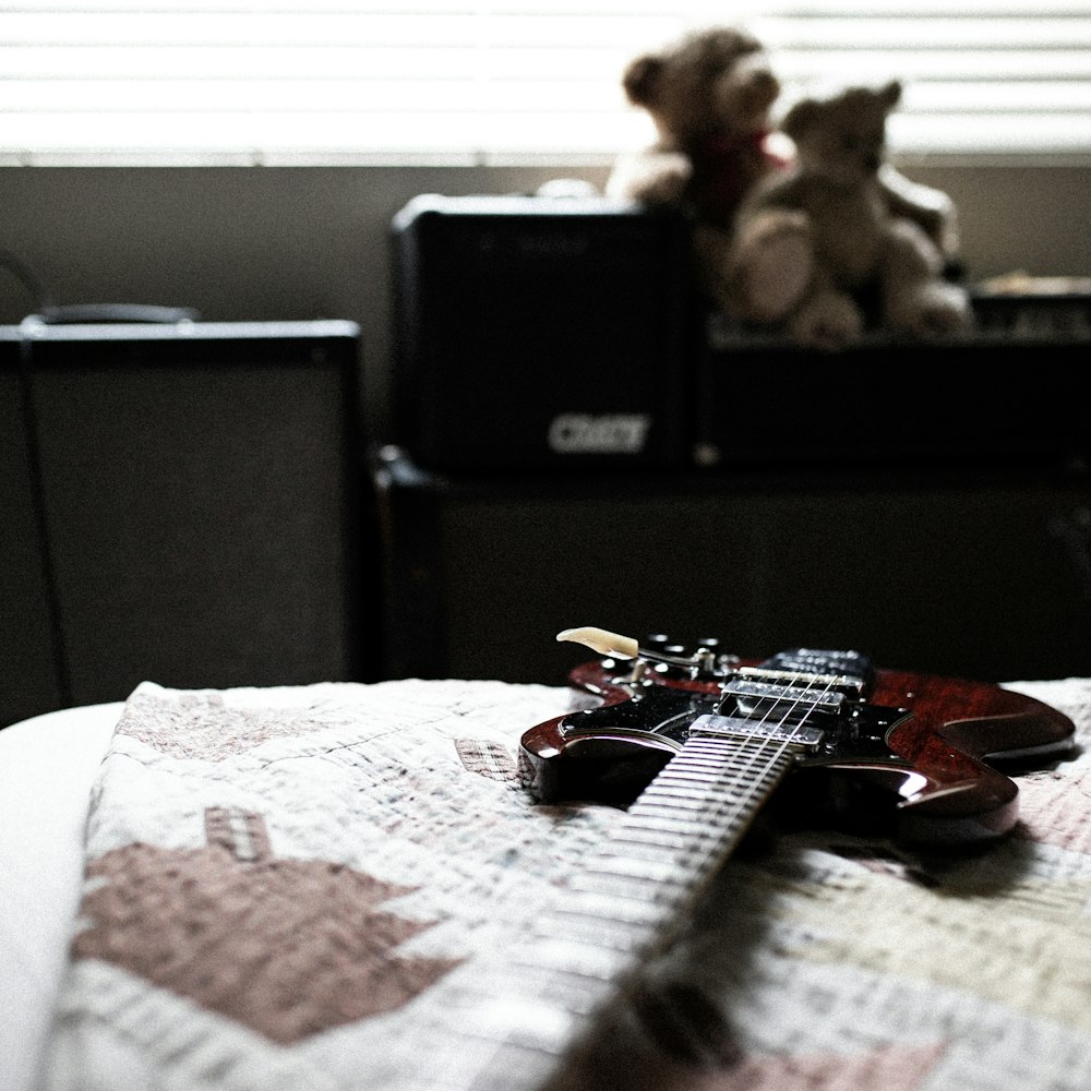 Una guitarra acostada encima de una cama junto a un oso de peluche