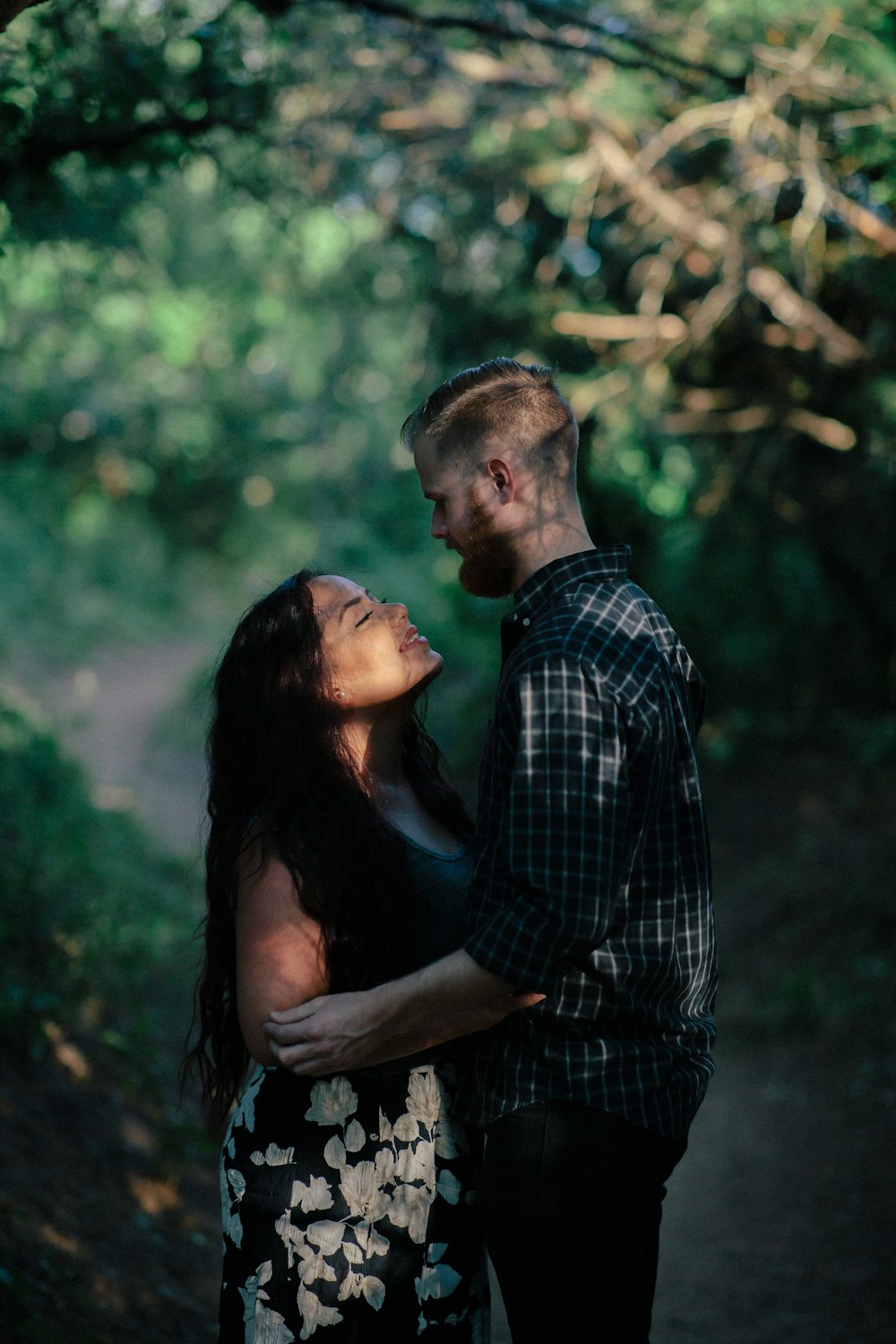 man hugging woman looking at each other surrounded by trees