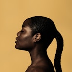 braided woman taking photo beside yellow painted wall