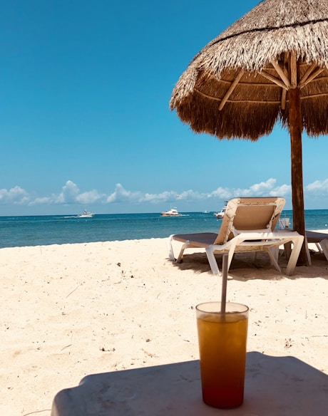 brown parasol and two beach chairs on beach sand