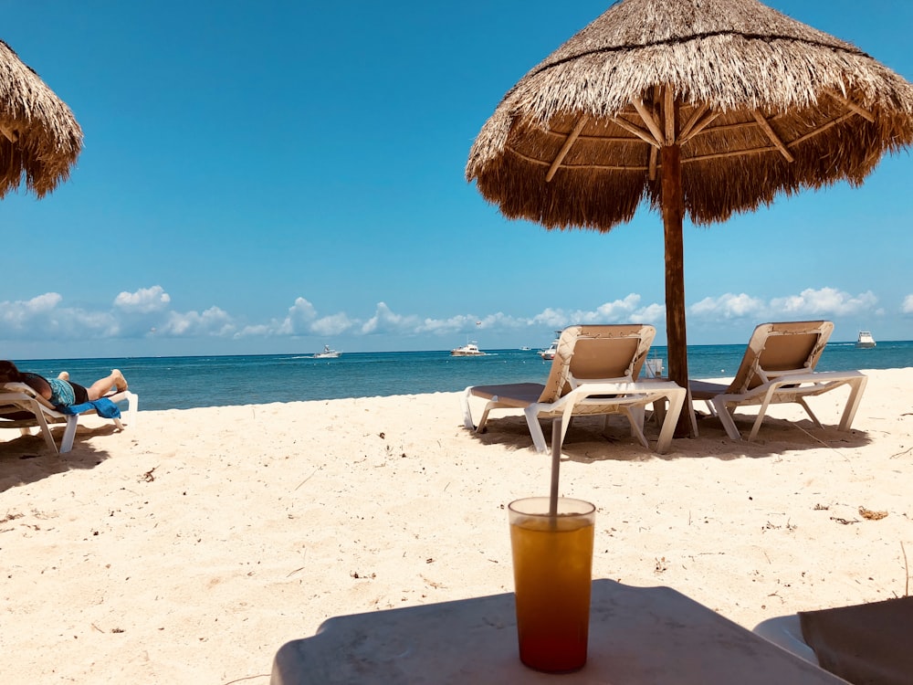 brauner Sonnenschirm und zwei Liegestühle im Strandsand