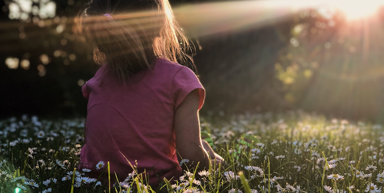 girl sitting on daisy flowerbed in forest