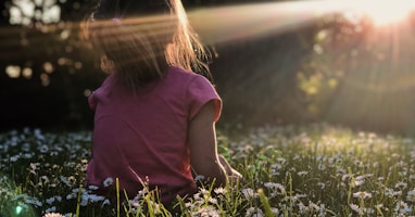 girl sitting on daisy flowerbed in forest