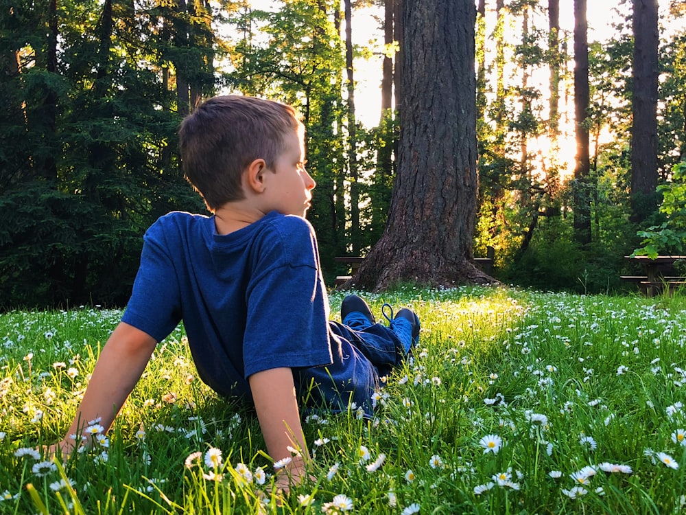 boy in blue t-shirt and blue shorts sitting on green grass field