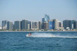 Sleek gold-accented jet ski gliding over dark waters at dusk with Dubai skyline in the background.