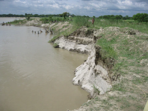 Researchers examining soil layers with scientific tools near a flowing river.