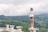 A woman wearing sunglasses and a t-shirt with the text 'Normal People Scare Me' stands confidently on a stone ledge surrounded by a lush, green forested landscape. The sky is cloudy, obscuring the sun, creating a serene yet adventurous atmosphere.