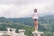 A woman wearing sunglasses and a t-shirt with the text 'Normal People Scare Me' stands confidently on a stone ledge surrounded by a lush, green forested landscape. The sky is cloudy, obscuring the sun, creating a serene yet adventurous atmosphere.