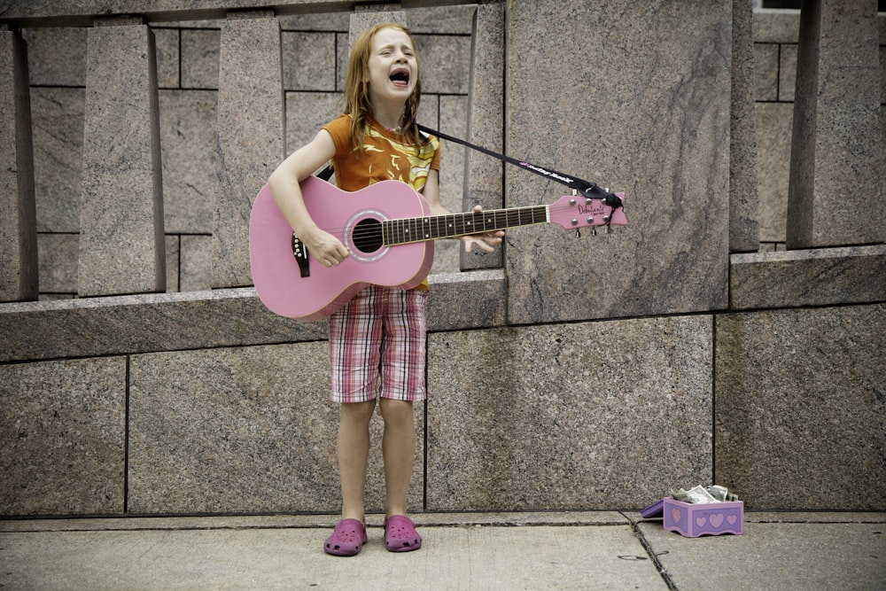 girl playing guitar near wall