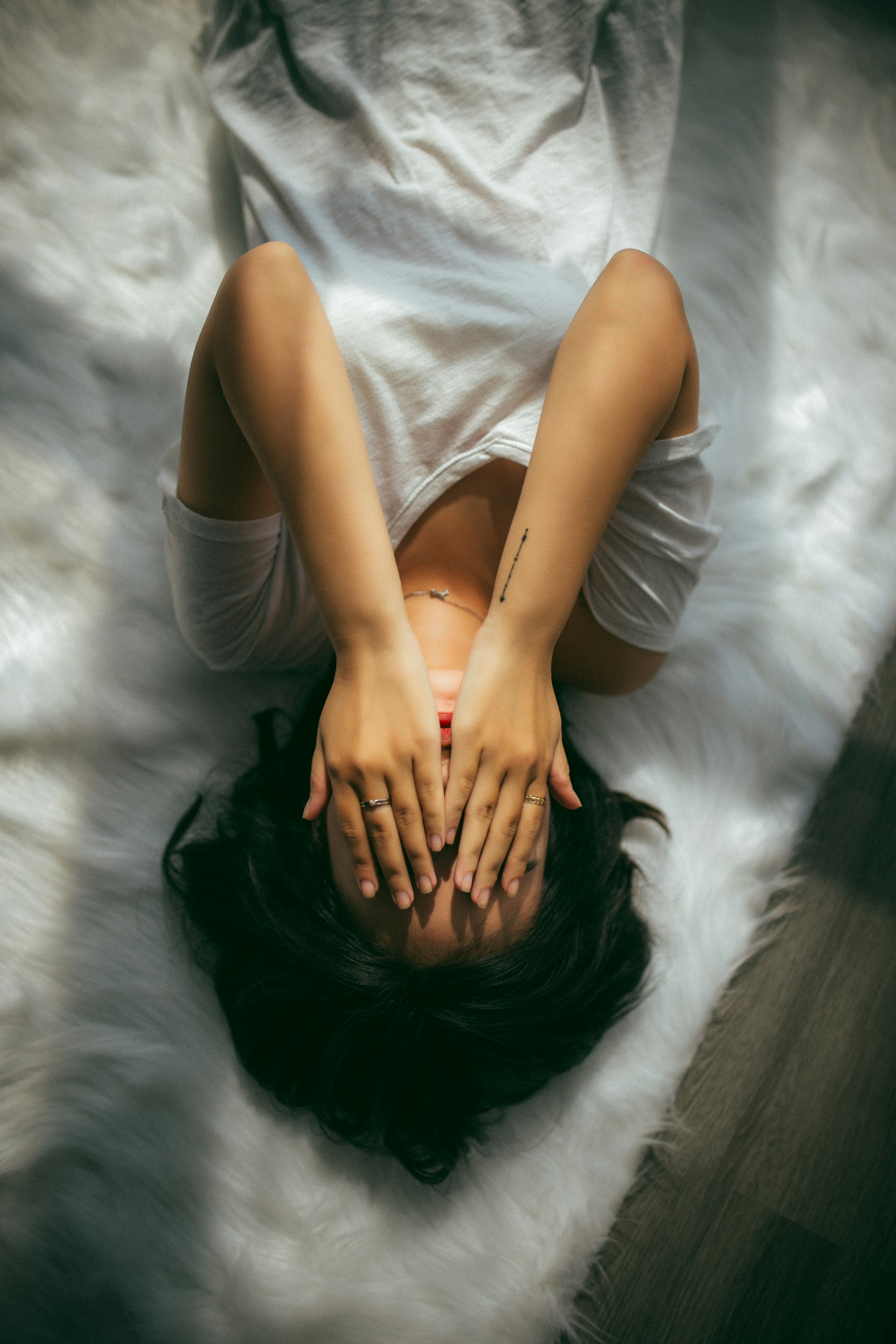 Woman lying on white bedding, hands covering her face symbolising ghosting of period.