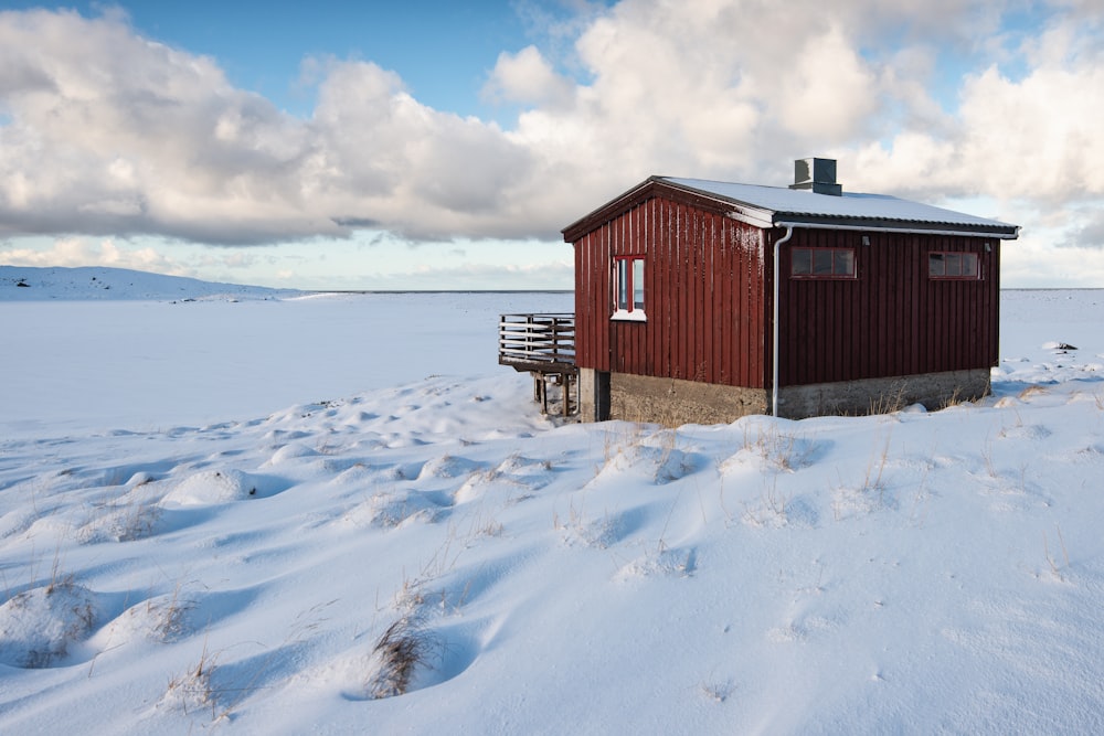 Cabane en bois rouge et marron sur un terrain recouvert de neige pendant la journée