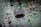 A close-up view of a green printed circuit board featuring a prominent black integrated circuit in the center. The board is populated with various small components such as resistors and capacitors, connected by silver traces. White alphanumeric markings are visible on the board's surface.