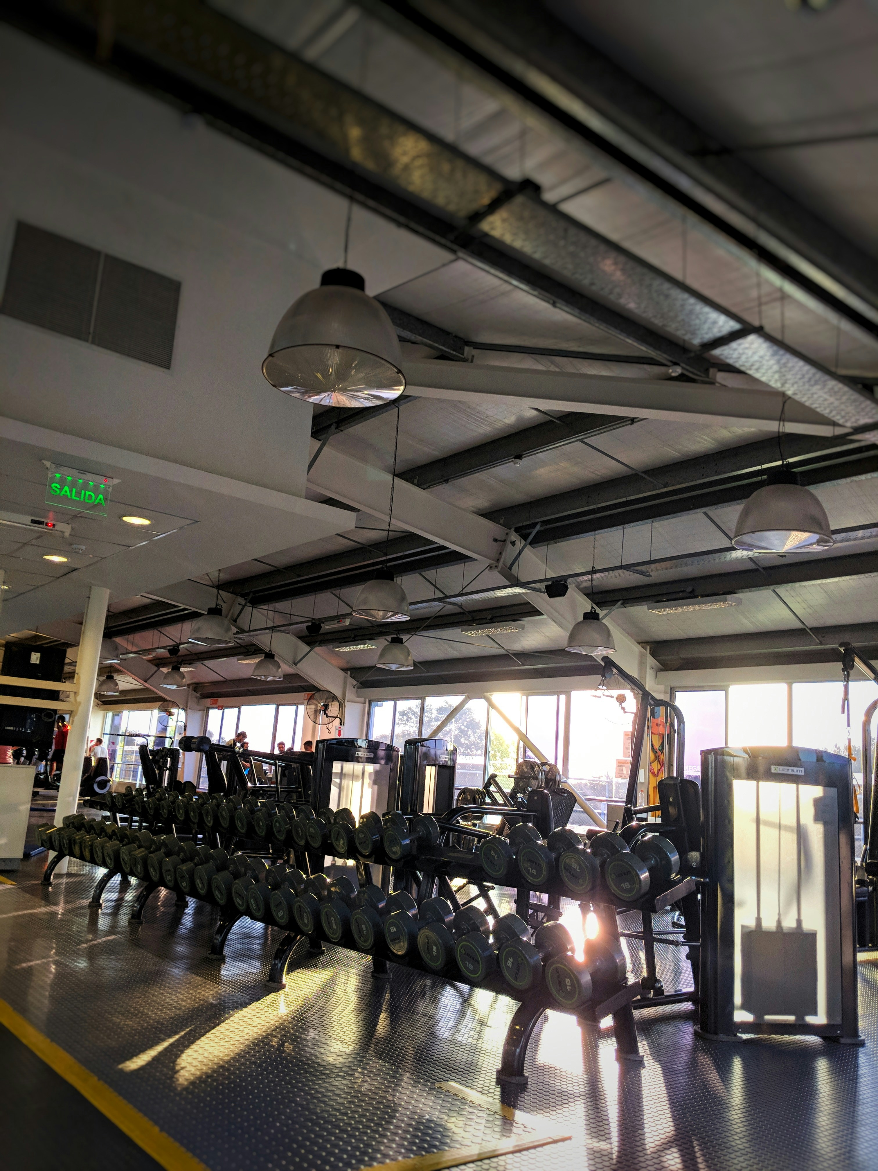 Sports equipment including dumbbells and yoga mat on bright gym floor, well-lit
