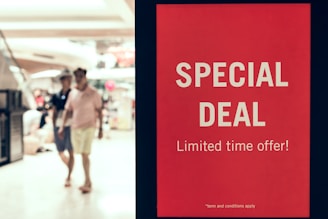 A red sign displays the words 'SPECIAL DEAL' and 'Limited time offer!' in bold white letters, standing prominently in a shopping mall setting. In the background, two people walk past the sign, out of focus.
