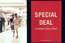 A red sign displays the words 'SPECIAL DEAL' and 'Limited time offer!' in bold white letters, standing prominently in a shopping mall setting. In the background, two people walk past the sign, out of focus.