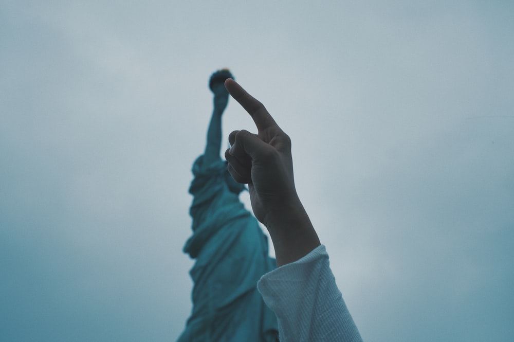 person's pointing finger pointing statue of liberty torch