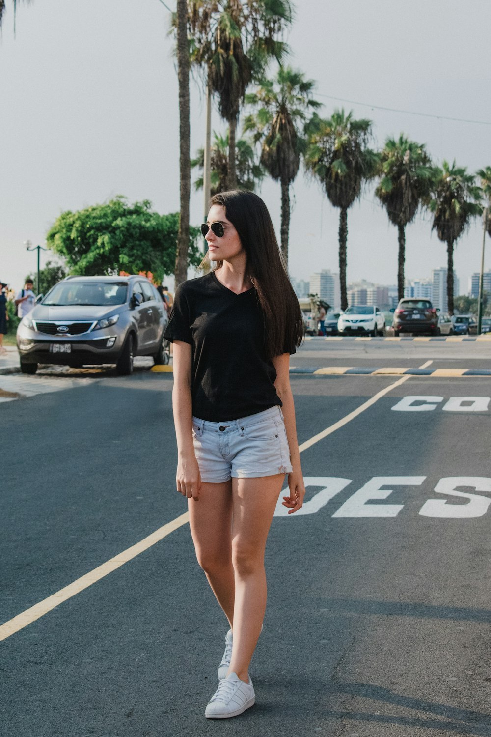 woman wearing black V-neck shirt and blue shorts standing on gray concrete road