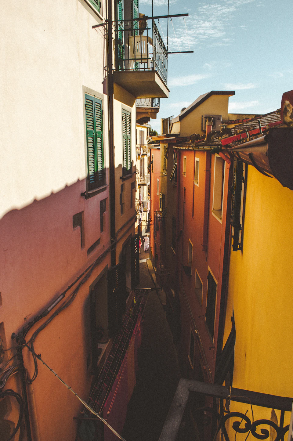 Narrow alleyway between two brightly colored buildings with balconies and clothesline hanging below