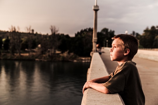 selective focus photo of boy at the bridge near body of water in Redding United States