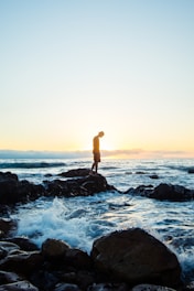 man standing on black rock formation in body of water