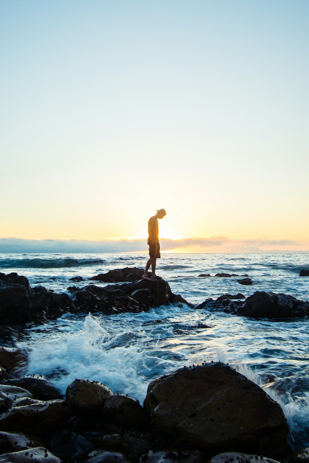 man standing on black rock formation in body of water