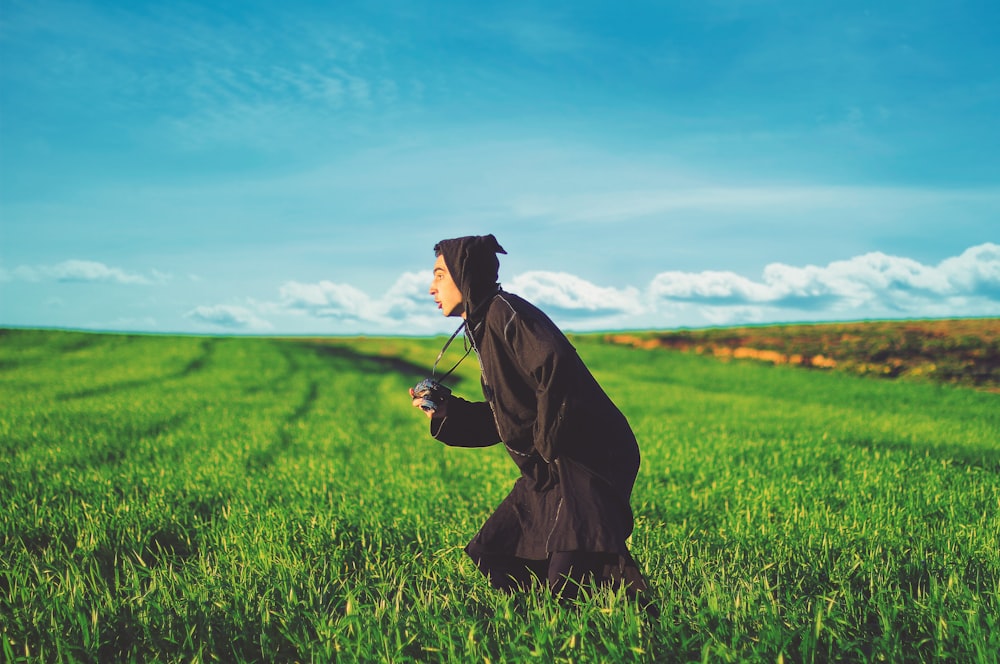 photography of man in black cloak running on grass field