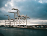 Cranes lifting heavy steel materials at a busy shipping dock under a steel grey sky.