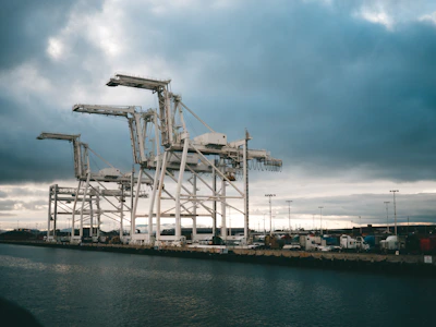 Dark photo of a busy international port with containers and cranes under moody lighting.