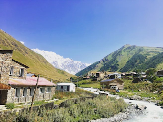 Charming stone cottages nestled in lush green Albanian mountains under a clear blue sky.