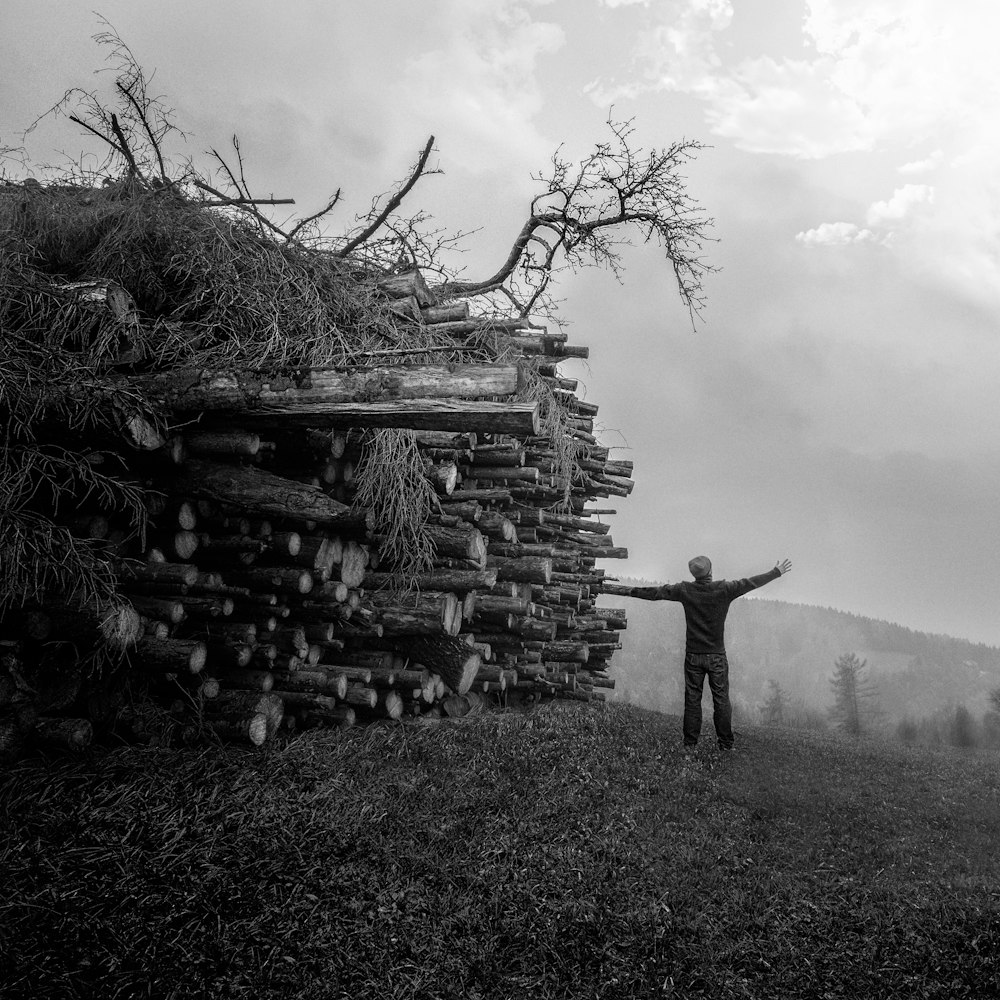 grayscale photography of man standing next to piles of woods