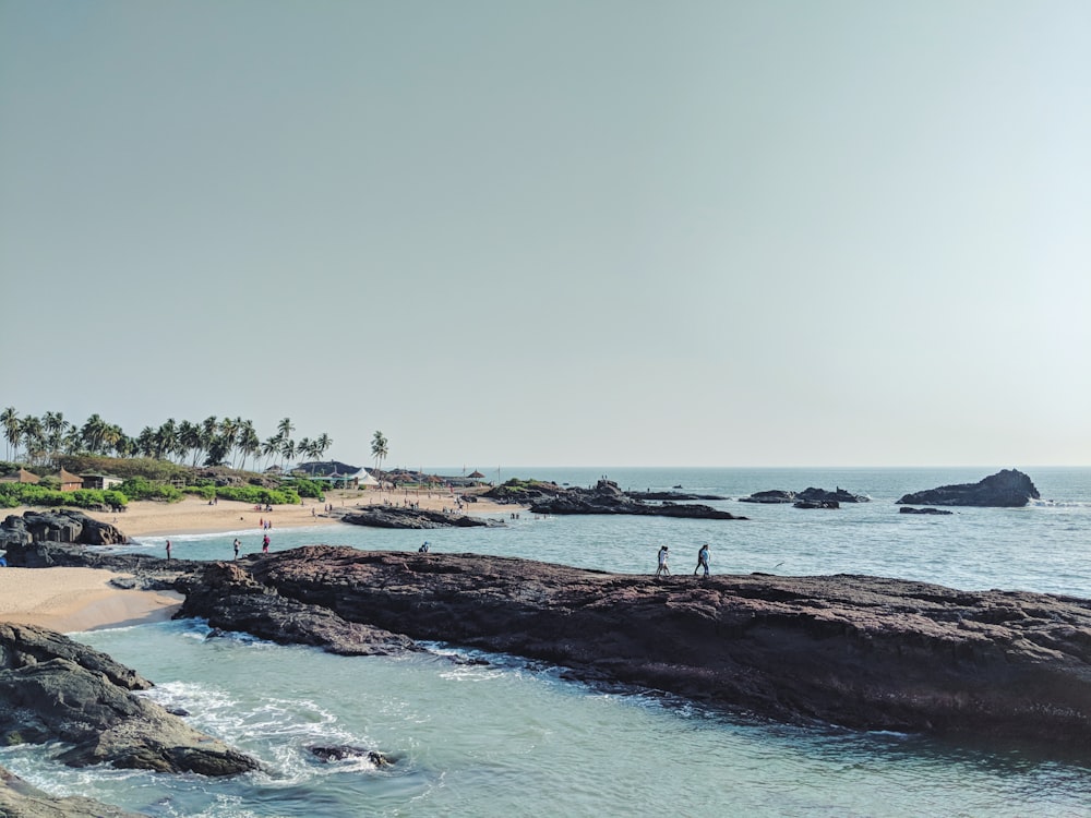 people walking on large rock monolith near sea