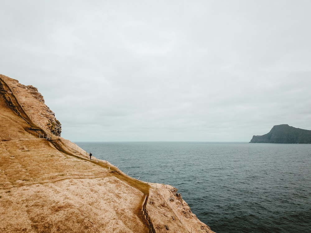 person standing on brown mountain in front of body of water