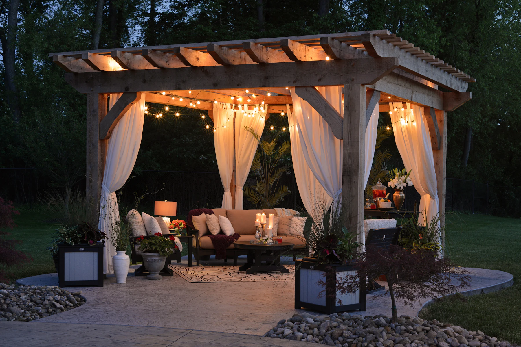 A garden gazebo hung with curtains and string lights at dusk
