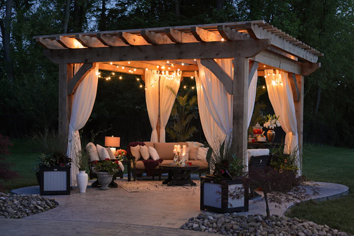 A garden gazebo hung with curtains and string lights at dusk