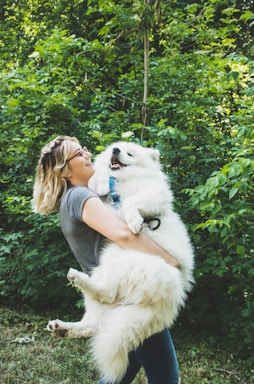 woman carrying long-coated white dog near green leafed plants