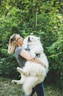 woman carrying long-coated white dog near green leafed plants