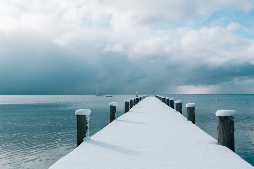 brown wooden dock covered with snow and body of water