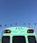 A turquoise bus with #NeverStress written on the back combines with the clear blue sky. Tall palm trees are seen in the background, suggesting a tropical or Californian setting.