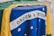 A close-up of the Brazilian flag displaying the green, yellow, and blue sections with white stars and the phrase 'Ordem e Progresso' prominently. The fabric appears to be slightly wrinkled, indicating it is draped over a surface.