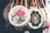 Circular woven handbags hang in a row, each with unique and colorful embroidery. The central bag features bold pink and white floral patterns, while another displays intricate geometric designs. Leather straps add a touch of contrast to the baskets.