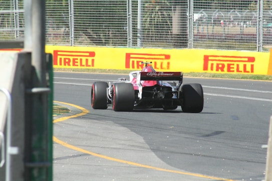 A Formula 1 race car with an Alfa Romeo logo on the rear drives down a track. The vehicle is surrounded by barriers and there is visible sponsorship branding from Pirelli along the yellow barriers. The car is mid-turn on an asphalt surface with visible rubber markings.