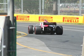 A Formula 1 race car with an Alfa Romeo logo on the rear drives down a track. The vehicle is surrounded by barriers and there is visible sponsorship branding from Pirelli along the yellow barriers. The car is mid-turn on an asphalt surface with visible rubber markings.