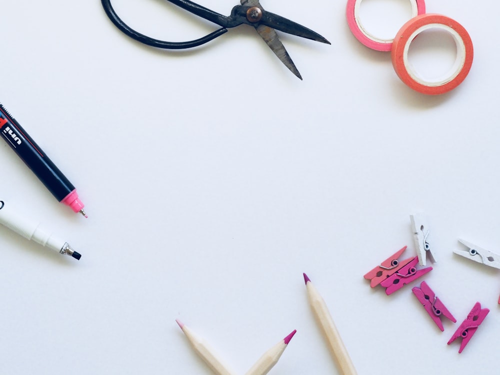 black scissors near brown pencils on top of white textile