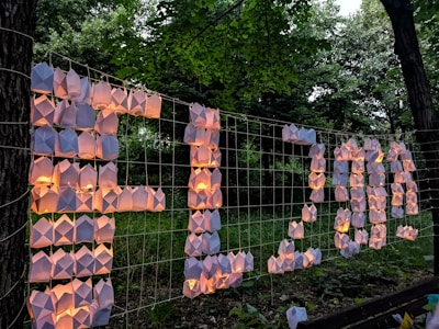 Origami lanterns arranged on a grid create an illuminated sign that reads FL2017. The scene is set against a background of lush green trees, indicating an outdoor setting.