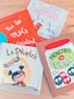 Four colorful children's books are arranged on a light wooden surface. Each book cover features distinct artwork and typography. One book has an orange cover with white lettering and small star designs. Another book has a blue and white cover with an illustration of an indigenous character. A third book displays an animated character with a furry costume on a primarily white cover. The fourth book has a cartoonish jar filled with bright-colored characters against a brownish background.