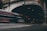 A motion-blurred red and silver bus speeds past an arched tunnel entrance. The tunnel is marked with a clearance sign, and there are various traffic signs including a speed limit sign. Dimly lit, the scene captures a sense of urban movement and transit.