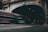 A motion-blurred red and silver bus speeds past an arched tunnel entrance. The tunnel is marked with a clearance sign, and there are various traffic signs including a speed limit sign. Dimly lit, the scene captures a sense of urban movement and transit.